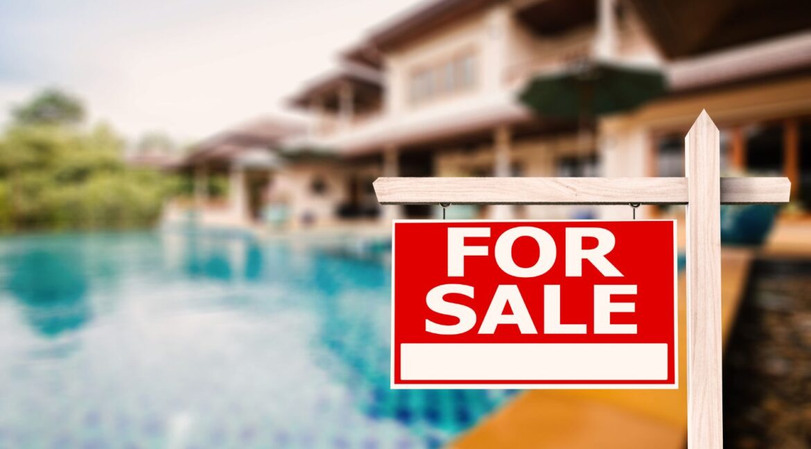 For Sale sign in front of a luxury home with a swimming pool in the background.