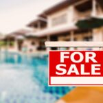For Sale sign in front of a luxury home with a swimming pool in the background.