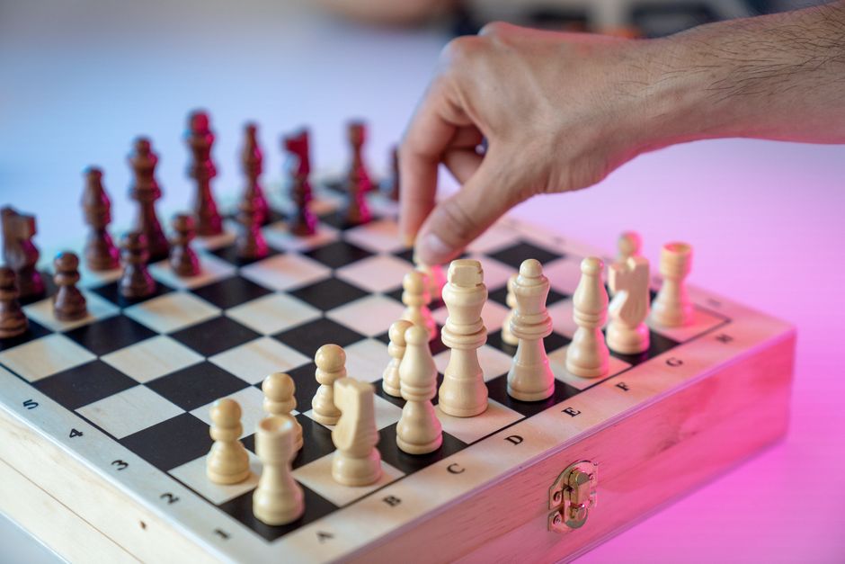 A close-up shot of a well-dressed person's hand strategically moving a chess piece on a modern, minimalist chess board, representing smart business moves.