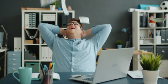 Business professional looks overwhelmed while working on a laptop at a modern desk, symbolizing the frustration and comple...